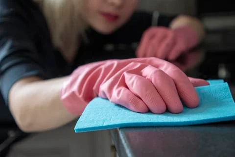 Beautiful blonde in rubber gloves and with a rag wipes dust from furniture Stock Photos