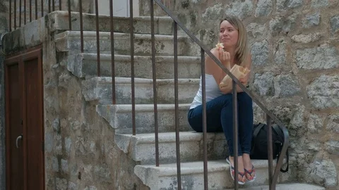Beautiful blonde sitting on the stone steps and eat a meal. Stock Footage 78205668