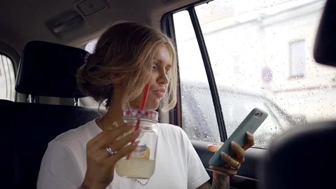 Beautiful blonde woman driving the car in the back seat texting with her friends Stock Footage