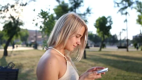 Beautiful blonde woman taking selfie using phone in city park Stock Footage 79793653