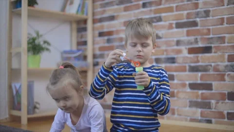 Beautiful boy is blowing soap bubbles and his sisters playing with them Stock Footage 102215358