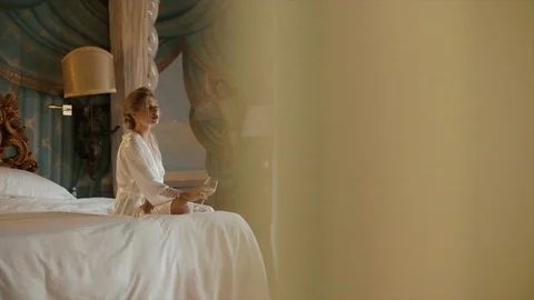 Beautiful Bride Is Sitting On The White Bed With A Glass Of Champagne. 스톡 동영상 106093483