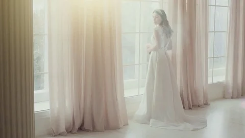 Beautiful bride standing at the large window and looking at the camera in a Video stock 73116635