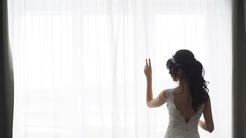 Beautiful bride standing at the window with curtains Stock Footage 76941610
