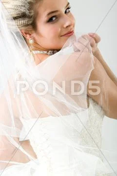 Beautiful bride staring over shoulder at camera holding veil Stock Photos