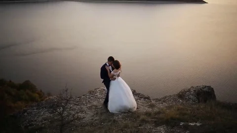 Beautiful bride wearing elegant white dress kissing her husband on the hill of Stock Footage 69147996