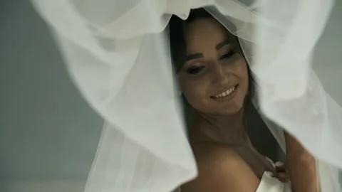 A beautiful bride in a wedding veil and bathrobe stands by the panoramic window Video stock 131843678