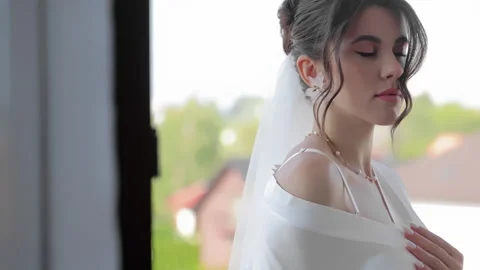 Beautiful bride in white gown posing near bright window with serene expression Video stock 301254464