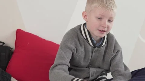 Beautiful brooding boy blond in a sweater sits at home on the couch Stock Footage 151885905