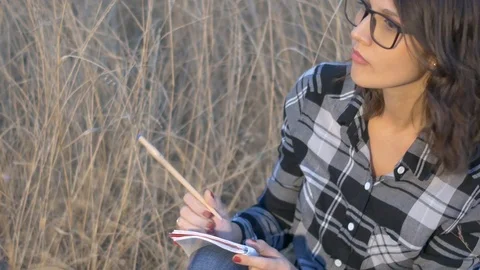 A beautiful, brooding girl with glasses writes in a notebook.Yellow field Video stock 116246124