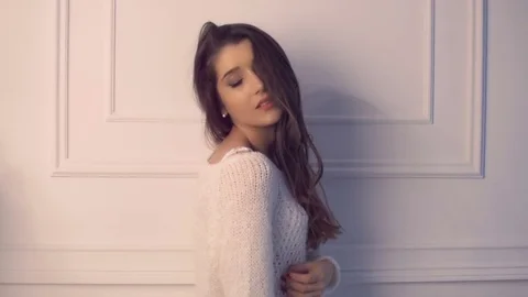 Beautiful brunette model flirting leaning back against white wall wearing white Stock Footage 70648008