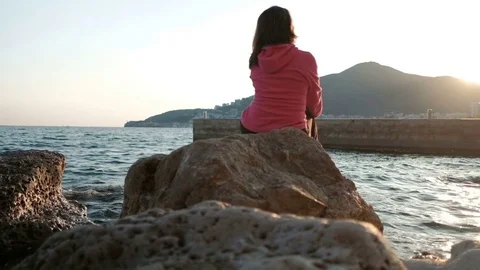 Beautiful brunette sits back on the rocks near lake in her travel. Stock Footage 76791655