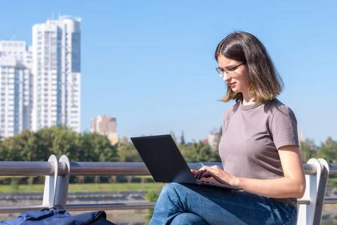 A beautiful brunette student with glasses is using a laptop on the street. A  Stock Photos