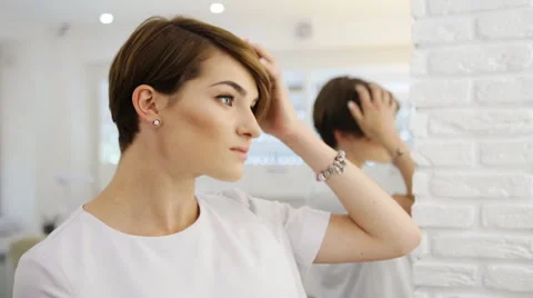 Beautiful brunette touching the ready short haircut in mirror. Concept of Stock Footage 64516809