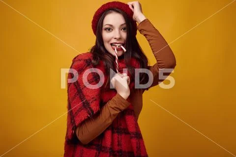 Beautiful brunette woman in red hat with big knitted scarf holding a candy Stock Photos