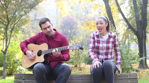 Beautiful brunette woman singing and man playing guitar in park Stock Footage 59556912