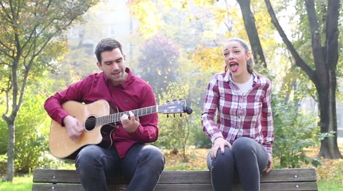 Beautiful brunette woman singing and man playing guitar in park Stock Footage 59556916