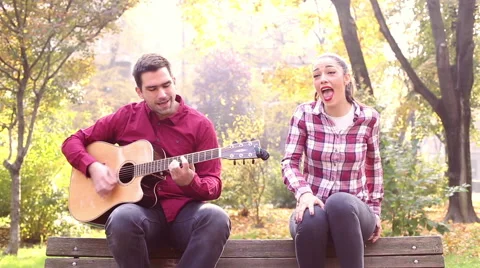 Beautiful brunette woman singing and man playing guitar in park Video stock 59556918