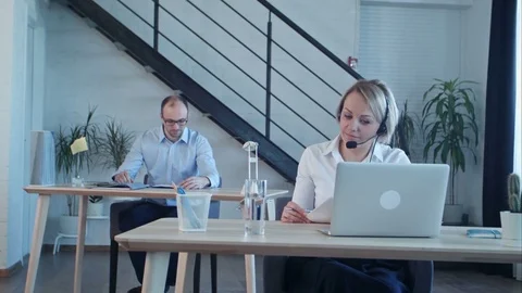 Beautiful call center agent having phone call and browsing the internet on her Vídeos de archivo 77421003