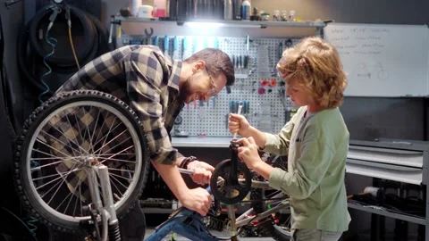 Beautiful caring skillful dad teaching cute little boy to fix bike in authentic Stock Footage 232493347
