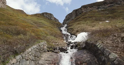 Beautiful cascading water flows down rocky terrain under cloudy skies in a Stockbeeldmateriaal 314082352