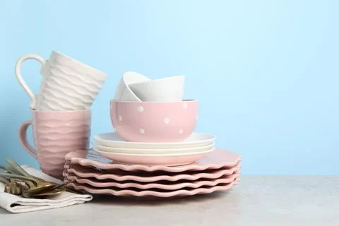 Beautiful ceramic dishware, cups and cutlery on light grey table, space for.. Stock Photos