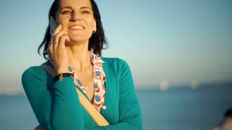 Beautiful chatting on cellphone while standing next to the seaside, steadycam sh Stock Footage