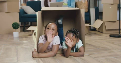 Beautiful cheerful small two dark-skinned girls playing inside in carton box and Stock Footage 150692376