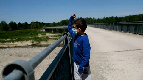 Beautiful child throws stones from the bridge into the river in phase 2 lockdown Stock Footage 130574875