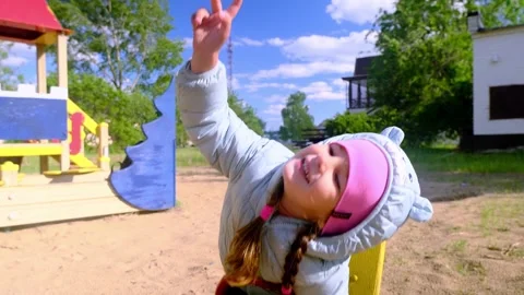 Beautiful child wearing a spring jacket and hat rides on balancing swing . Littl Stock Footage 277439216