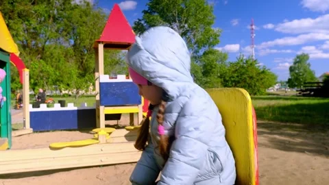 Beautiful child wearing a spring jacket and hat rides on balancing swing . Littl Stock Footage 278053980