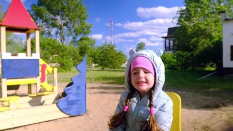 Beautiful child wearing a spring jacket and hat rides on balancing swing . Littl Stock Footage 279073585
