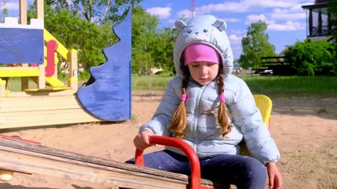 Beautiful child wearing a spring jacket and hat rides on balancing swing . Littl Stock Footage 279874361