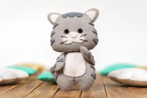 Beautiful children's toy. Gray kitty made of felt on a wooden background. Stock Photos