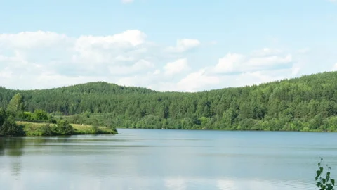 Beautiful clouds move over a body of water and wooded mountains on a summer Stock Footage 202645254