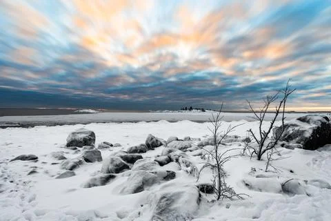 A beautiful cloudscape of dramatic evening sky and snow covered half frozen l Stock Photos