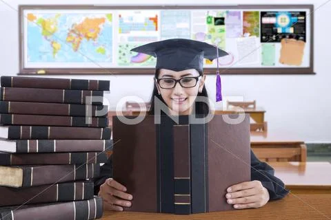 Beautiful college student with mortarboard reads books Stock Photos