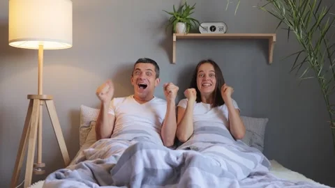 Beautiful couple lying in comfy bed enjoying movie joyfully smiling together in 库存影片 252822609