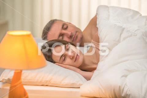 The beautiful couple sleeping on the bed on the background of a bedside lamp Stock Photos