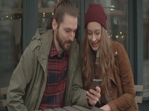 Beautiful couple with smartphone sitting in outdoors restaurant. Stock Footage 84827853