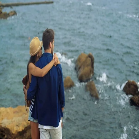 Beautiful couple standing on the stone and watching waves made by heavy wind Stock Footage 69294355