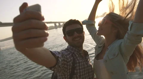Beautiful couple taking self portrait using smartphone by the river Видео 68079009