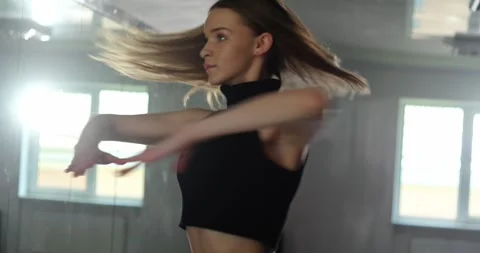 A beautiful dancer practices a dance in front of a mirror wall in the studio. Video stock 280479694
