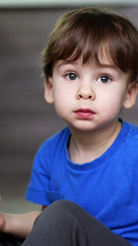 Beautiful dark-haired baby boy in blue t-shirt sits on the floor. Small kid eats Stock Footage 342249288