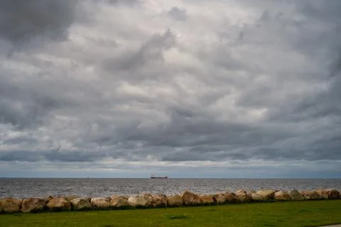 A beautiful, dramatic sky over the ocean. A lawn and stones in a wave breaker in Stock Photos