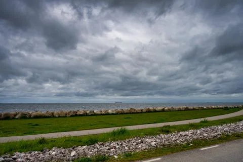 A beautiful, dramatic sky over the ocean. A lawn and stones in a wave breaker in Stock Photos