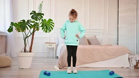 Beautiful elementary school girl performs sports exercises at home on a mat with Video stock 194514459