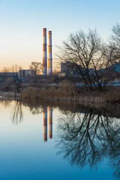 A beautiful evening cityscape with a reflection of trees and tall pipes in a Stock Photos