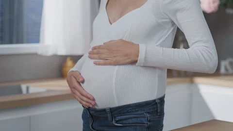 A beautiful expecting mother lovingly cradling her baby bump inside her modern Stock Footage 316033527