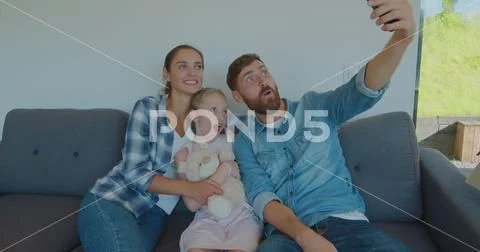 Beautiful family making memorable selfies on smartphone while relaxing, sitting Stock Photos
